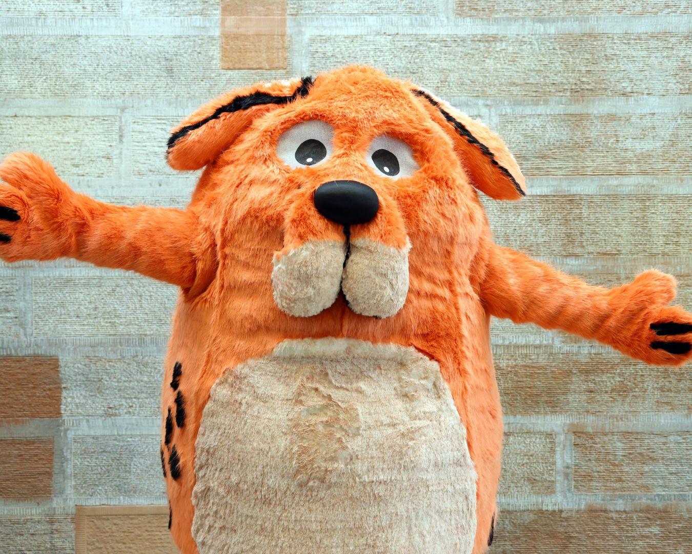 Children's Book Festival mascot Big Dog, predominantly orange with a white stomach and large floppy ears.