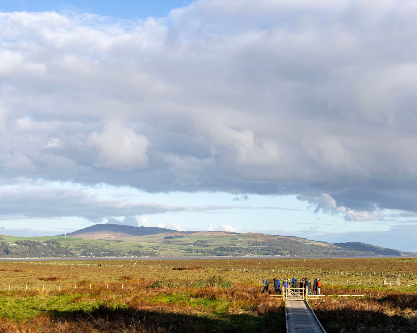 Sweeping vista of Wigtown Bay with a group of festival visitors stood at the end of a wooden walkway.