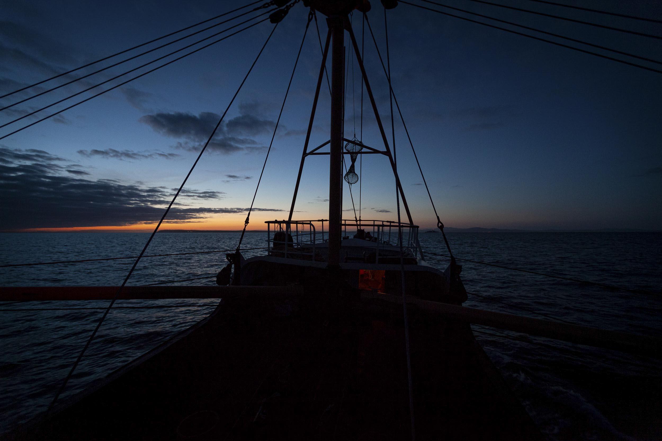 A fishing vessel out at sea as the sun is setting.