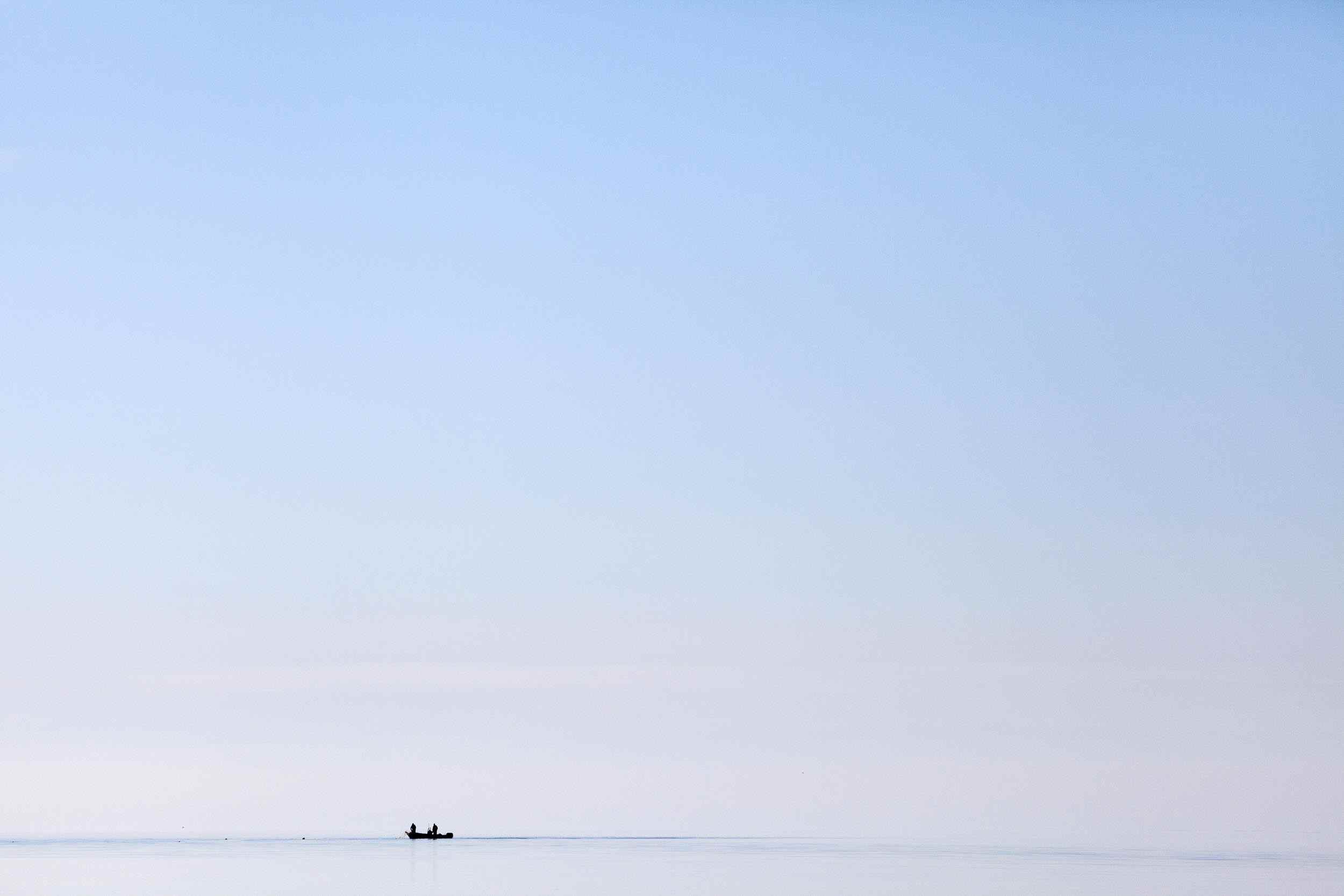 A small fishing boat on the horizon of a calm sea.