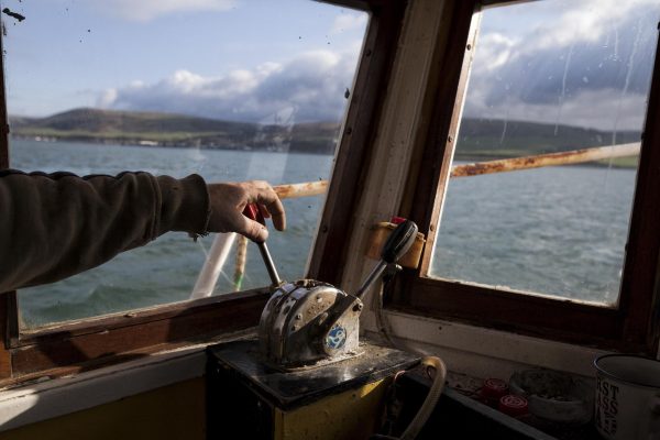 A hand is resting on the boat throttle of a fishing vessel out to sea.