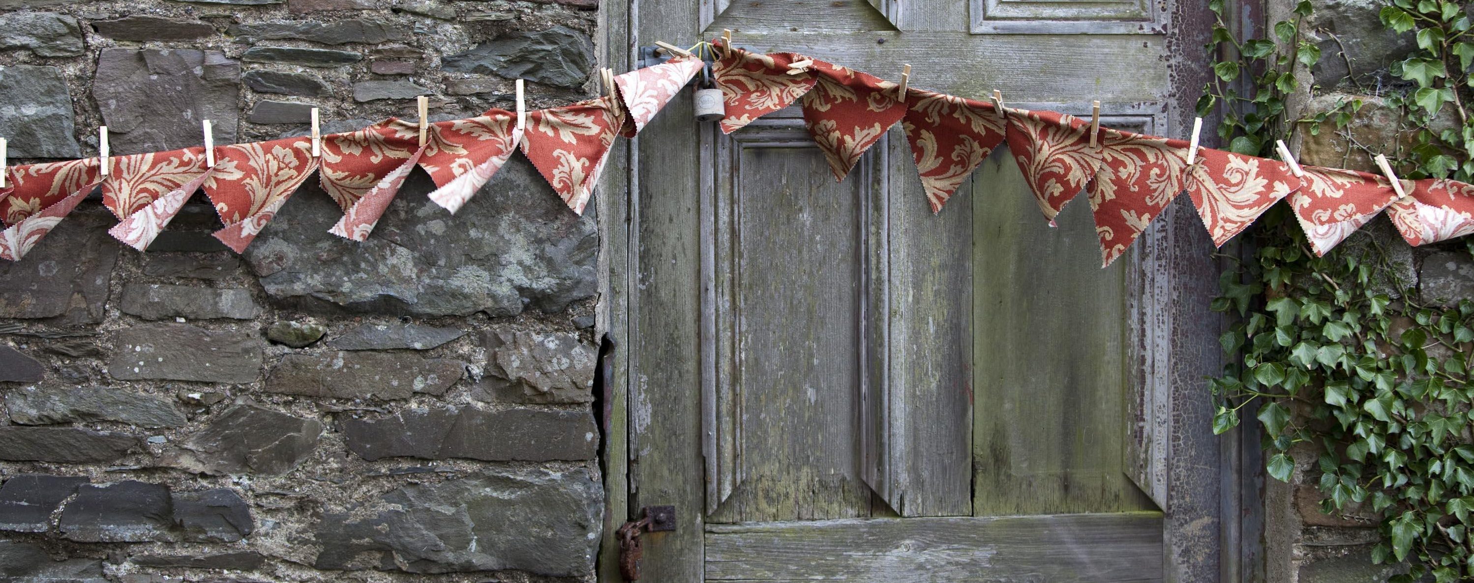 Red bunting hanging over a stone wall and old unpainted door. Ivy climbing up the wall.