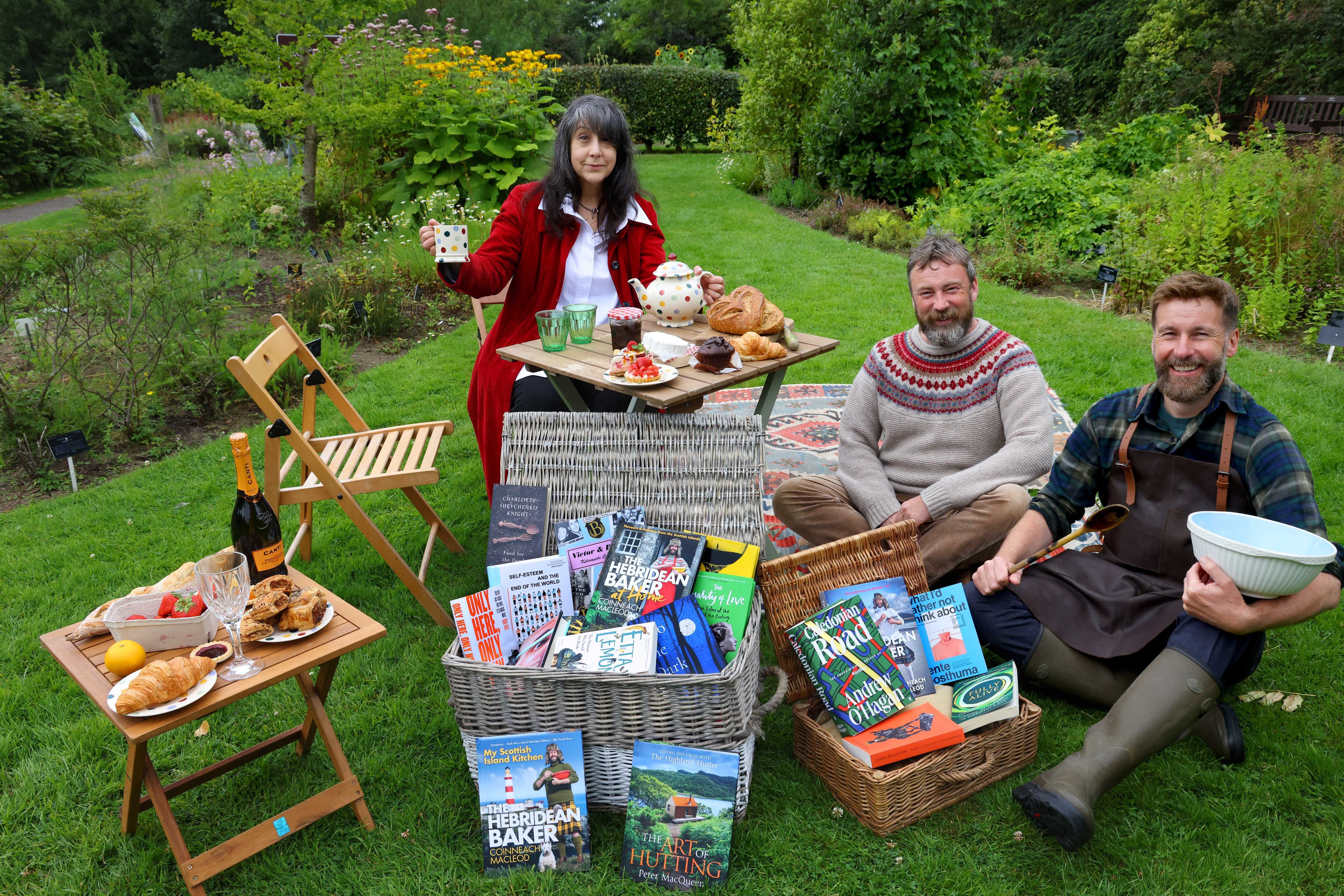 WBF 2024 Programme Launch PR image. Lee Randall, Peter MacQueen and Coinneach MacLeod at a picnic surrounded by baked goods and books.