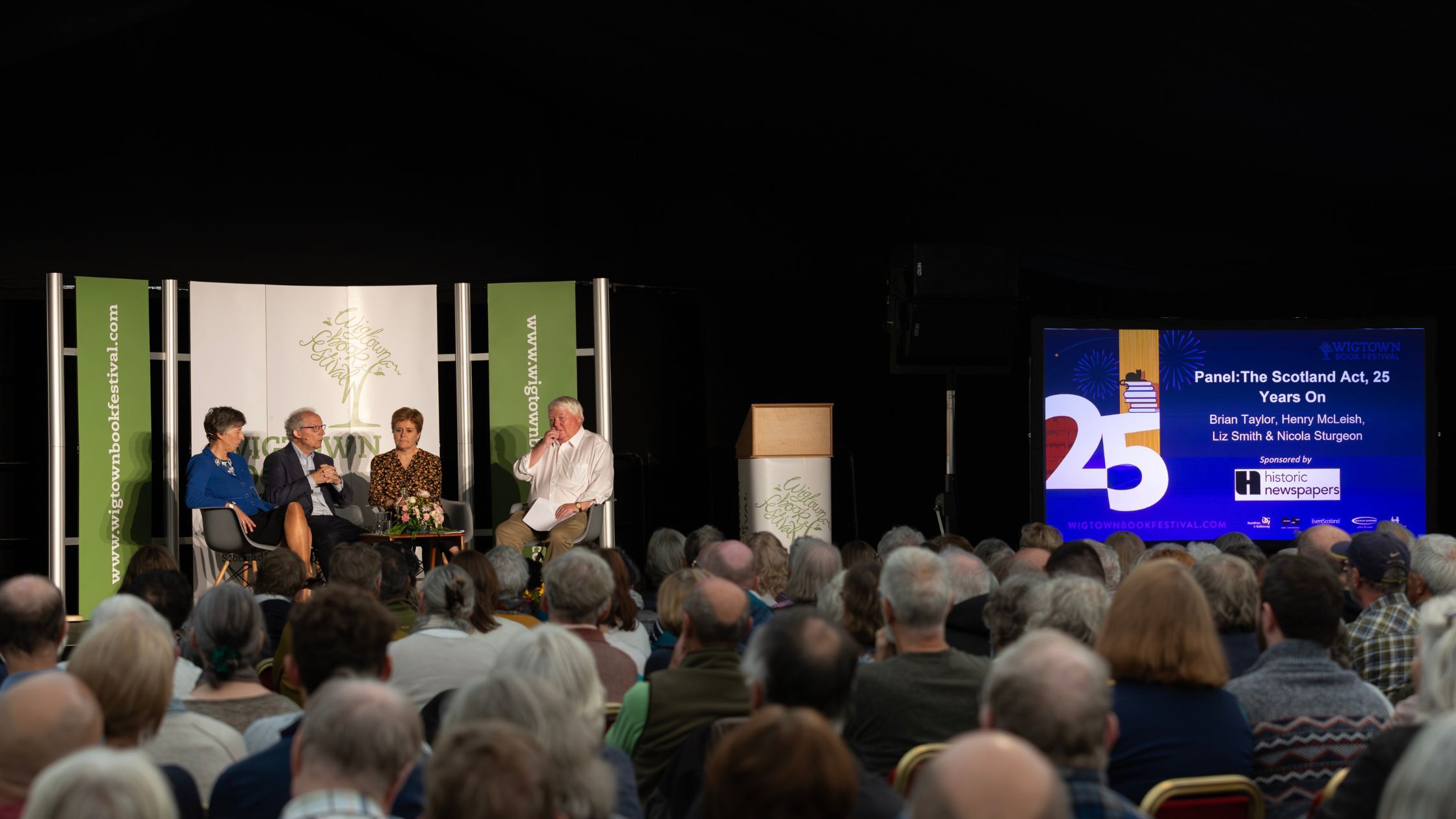 Left to right: Liz Smith, Henry McLeish, Nicola Sturgeon and Brian Taylor on stage at Wigtown Book Festival, with audience in foreground.