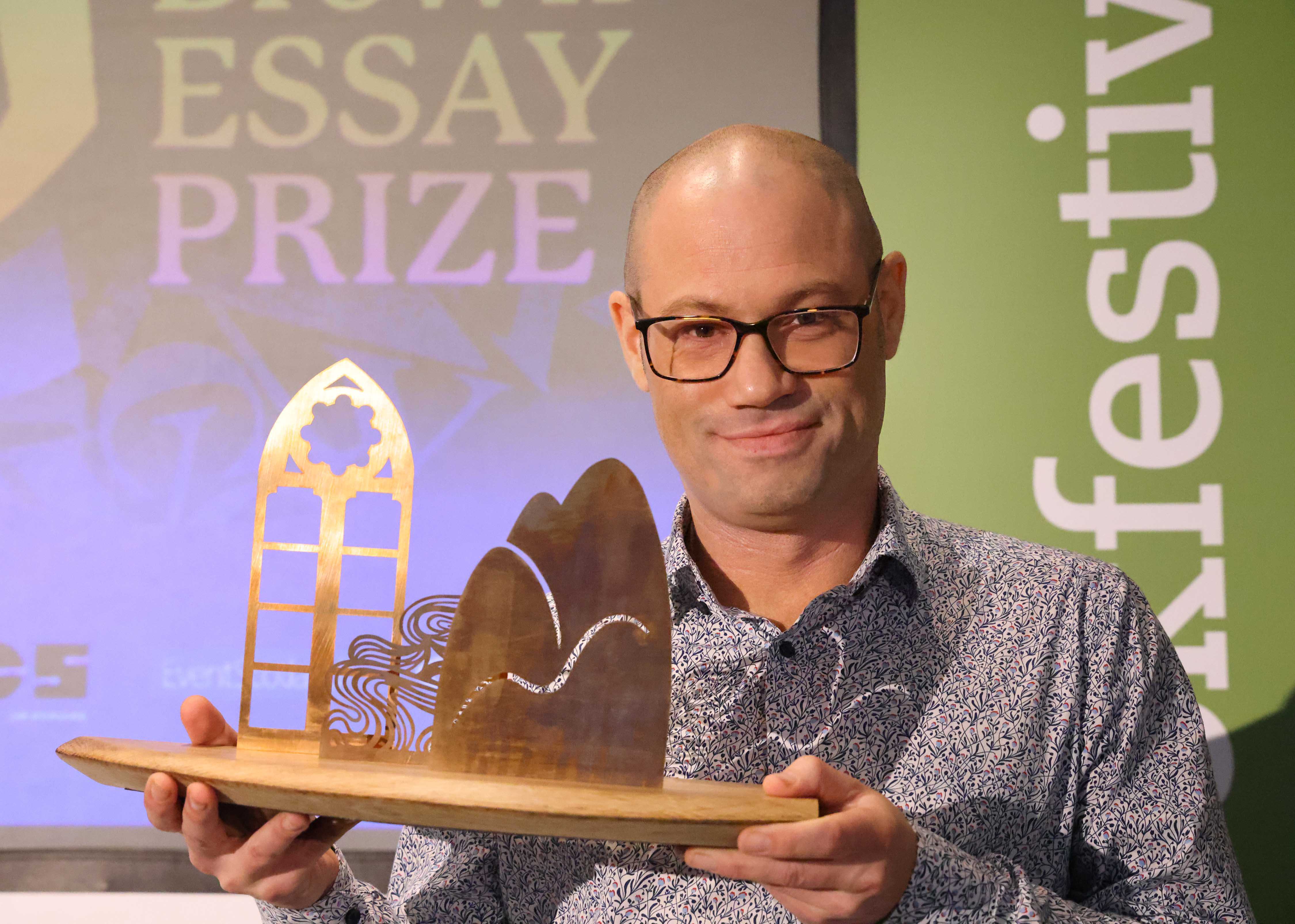 Anne Brown Prize Winner Rodge Glass holding his trophy on stage at the Wigtown Book Festival.