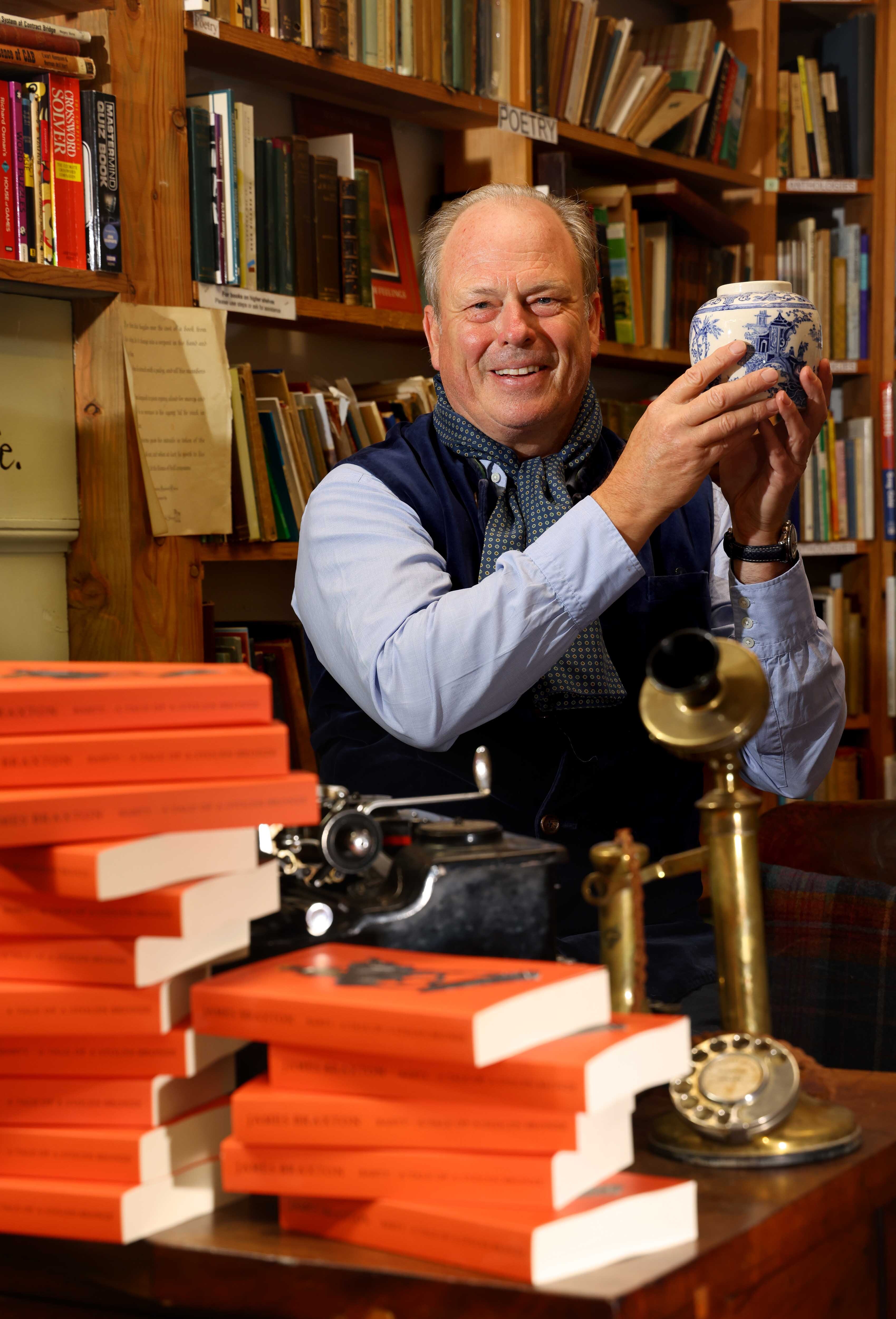 James Braxton in a bookshop, holding up a blue and white antique vase