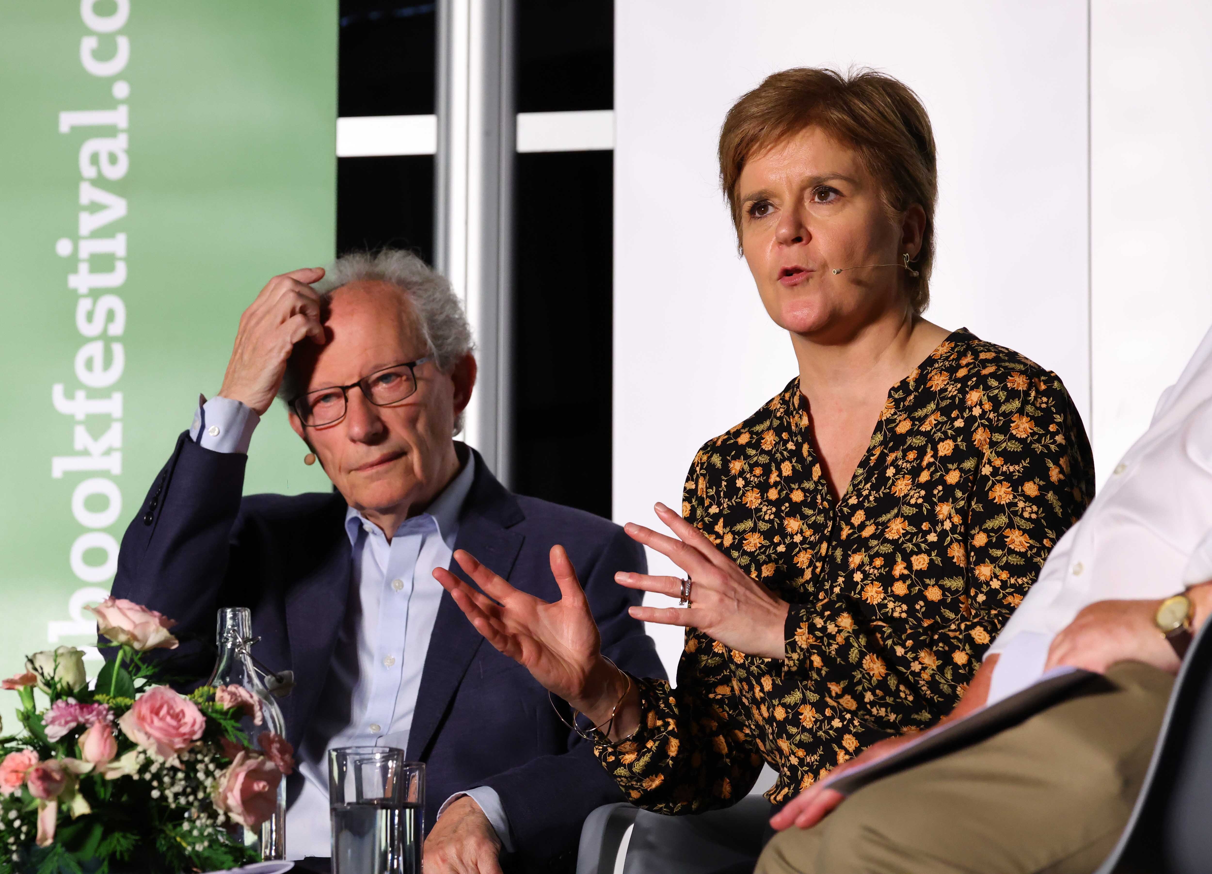 Henry McLeish and Nicola Sturgeon seated on stage at Wigtown Book Festival. McLeish scratches his head, Sturgeon gestures with her hands while speaking.