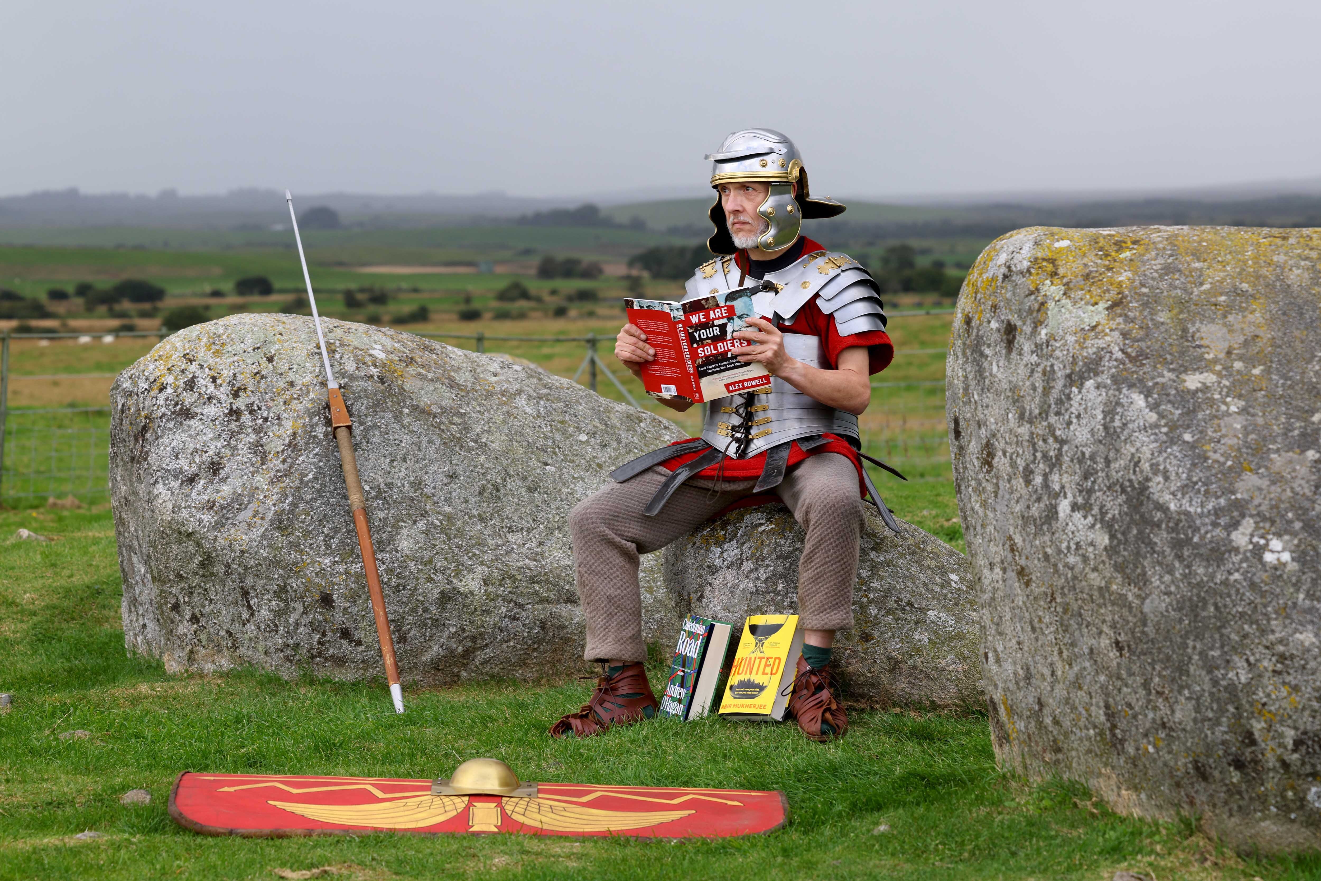 Matthew Shelley dressed as a Roman centurion, has laid down his spear and shield to read 2024 Wigtown Book Festival titles.