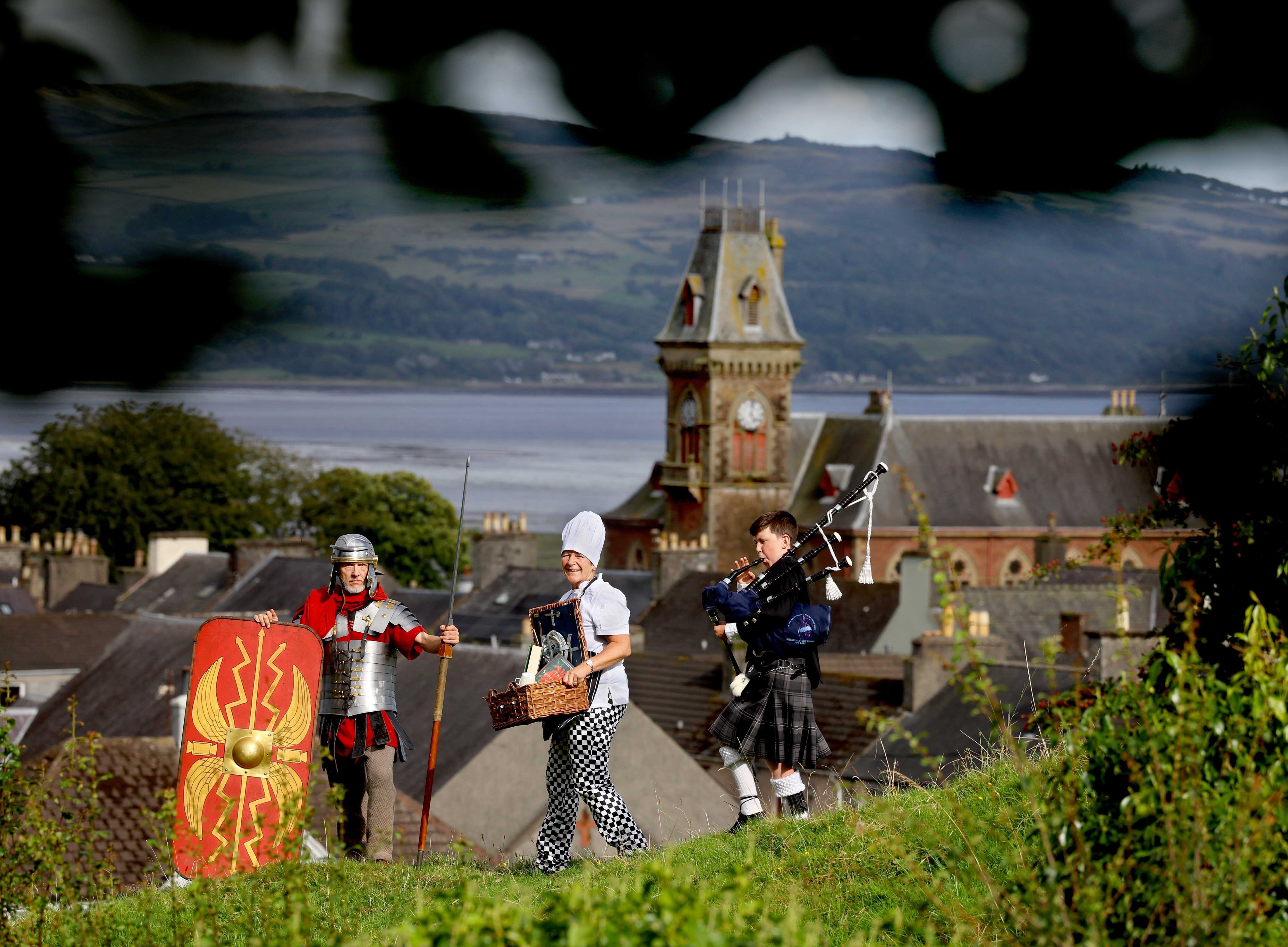 Matthew Shelley dressed as a Roman centurion, a Wigtown resident dressed as a chef and a bagpiper, in procession with a backdrop of Wigtown.