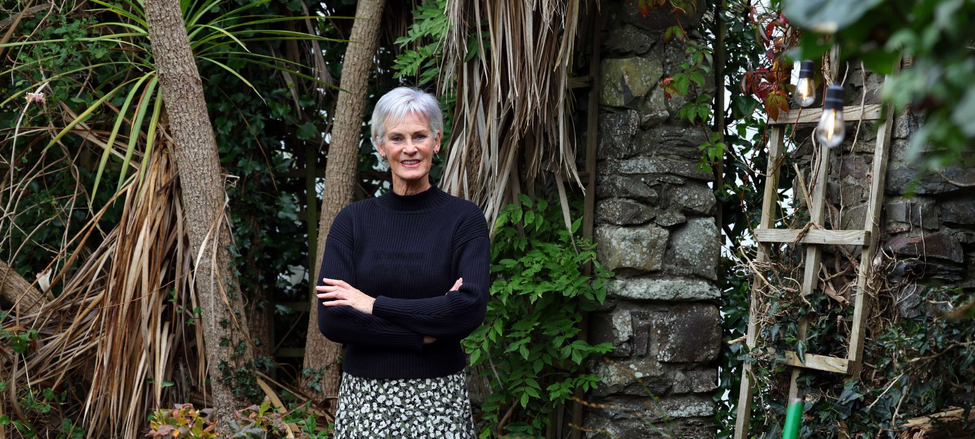 Judy Murray stands in a garden, arms folded.
