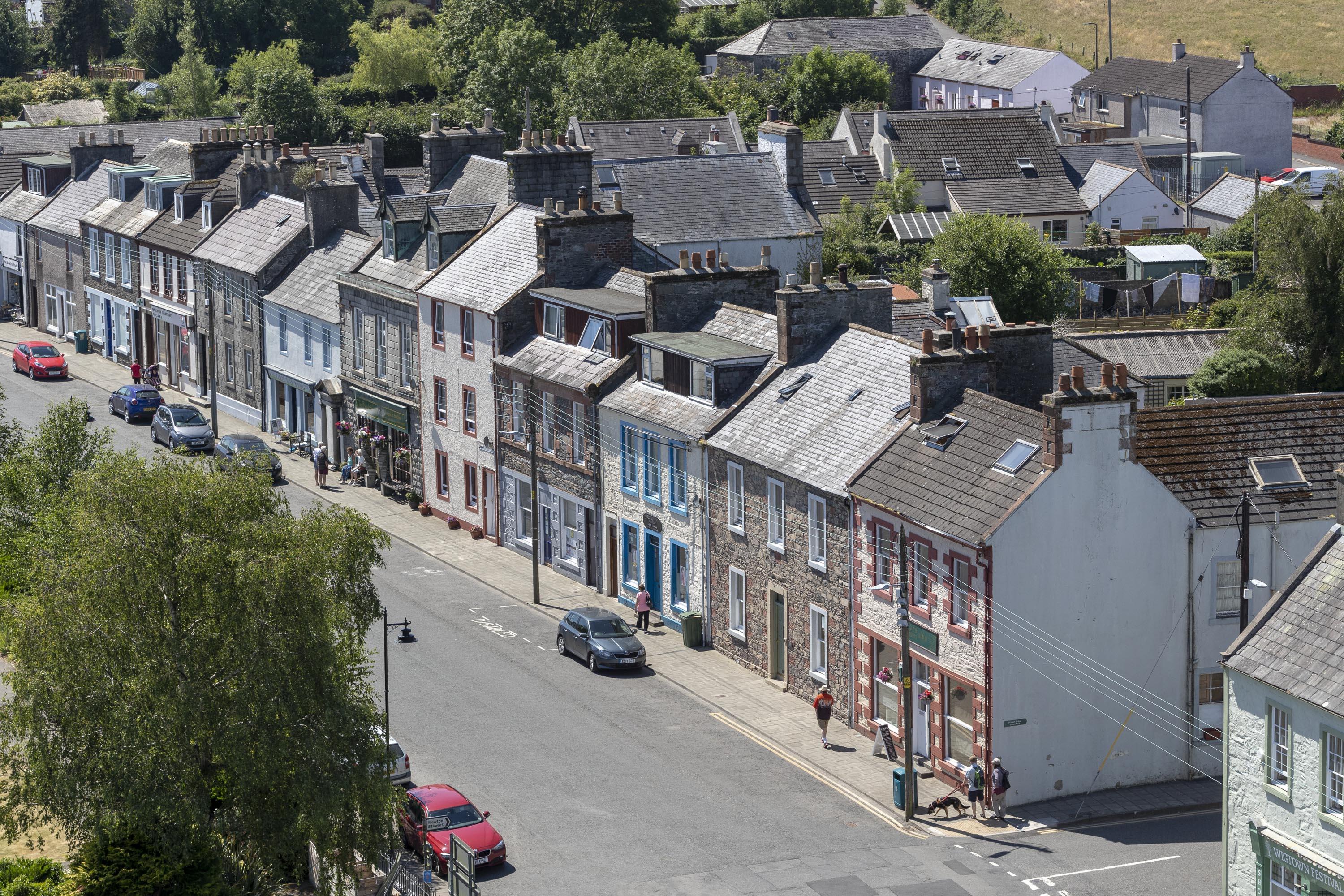 An aerial view of North Main Street, Wigtown, Scotland's National Book Town. Terraced houses and shops in various colours, trees in the forefront.