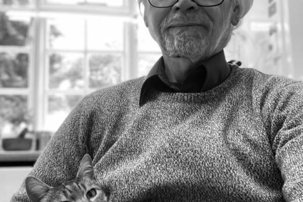 Larry Winger sitting in a chair holding a cat. Large windows behind him.