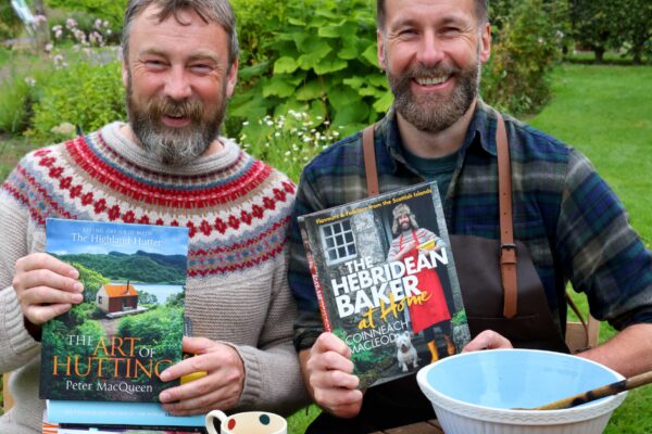 Peter MacQueen and Coinneach MacLeod holding their books "The Art of Hutting" and "The Hebridean Baker at Home", both smiling at the camera.