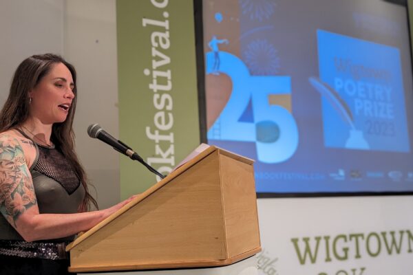 Keeks Mc, runner-up of the Wigtown Scots Poetry Prize reads at a lectern on stage at Wigtown Book Festival 2023