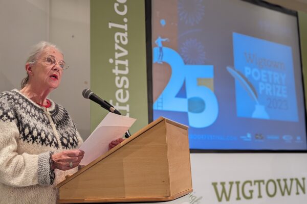 Stephanie Green is standing at a podium, holding a piece of paper and talking during the Wigtown Poetry Prize in 2023, part of the Wigtown Book Festival.