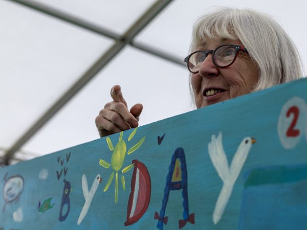 At a children's book event a volunteer holds up an illustrated banner with hand drawn lettering. In shot it says 'by day'.