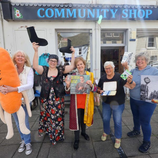 Wigtown Community Shop volunteers with festival chair Cathy Agnew, holding objects from the shop, stood in front of the community shop.