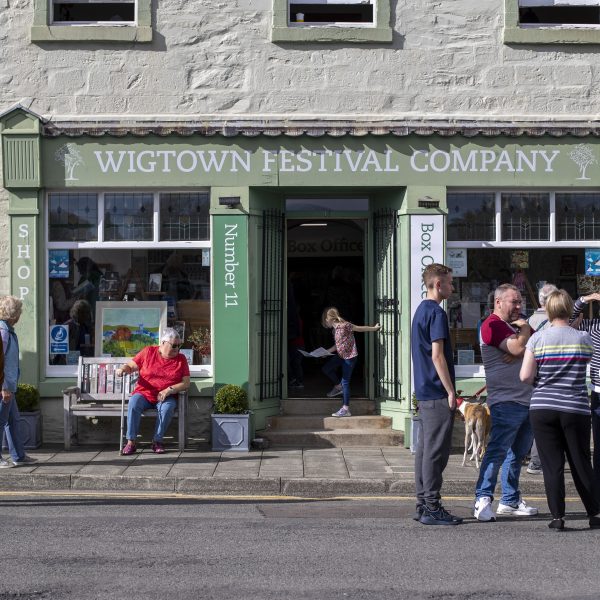 No.11 North Main St, Wigtown, home of the Wigtown Festival Company. People standing outside and talking in the sunshine during the Wigtown Book Festival. Young child entering the doorway with a piece of paper in her hand.