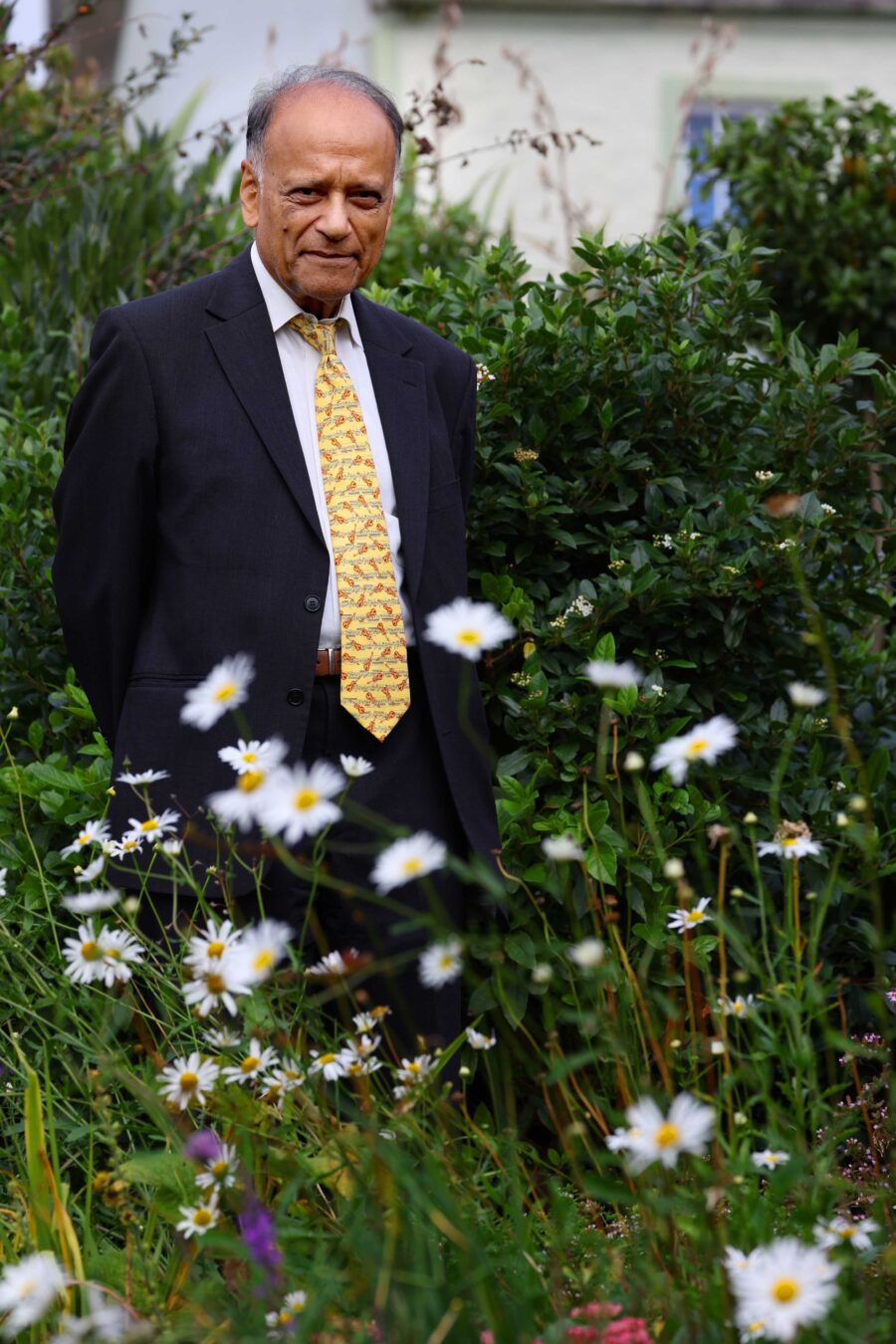 Professor Sir Partha Dasgupta in Wigtown Gardens, white flowers in the foreground.