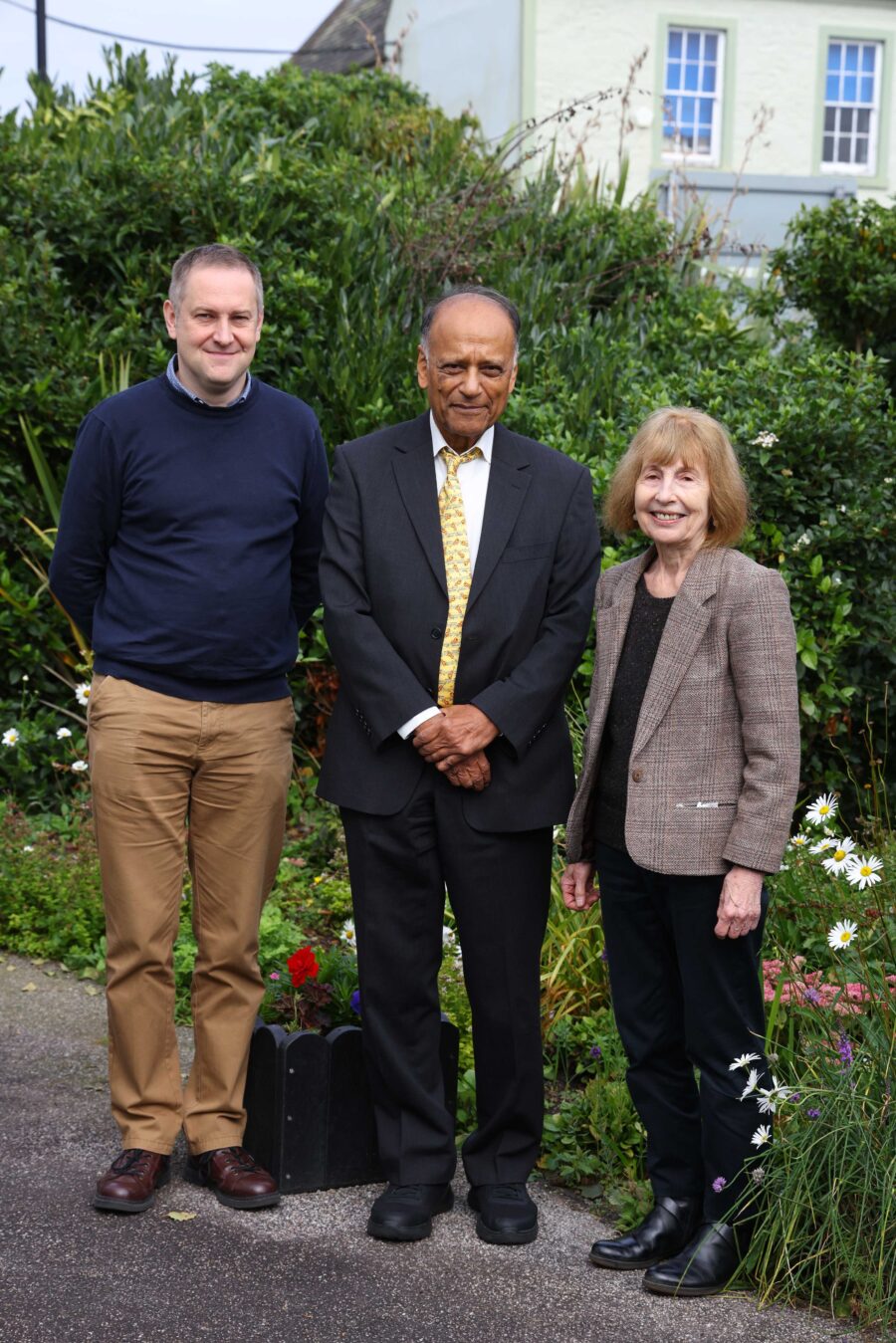 Professor Sir Partha Dasgupta stands in Wigtown Gardens with two other people.