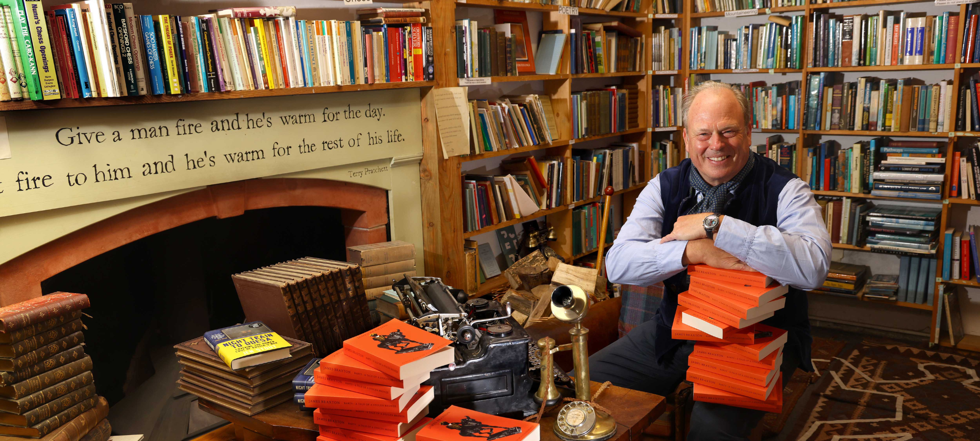 Portrait of James Braxton in a bookshop, holding a stack of his new books.